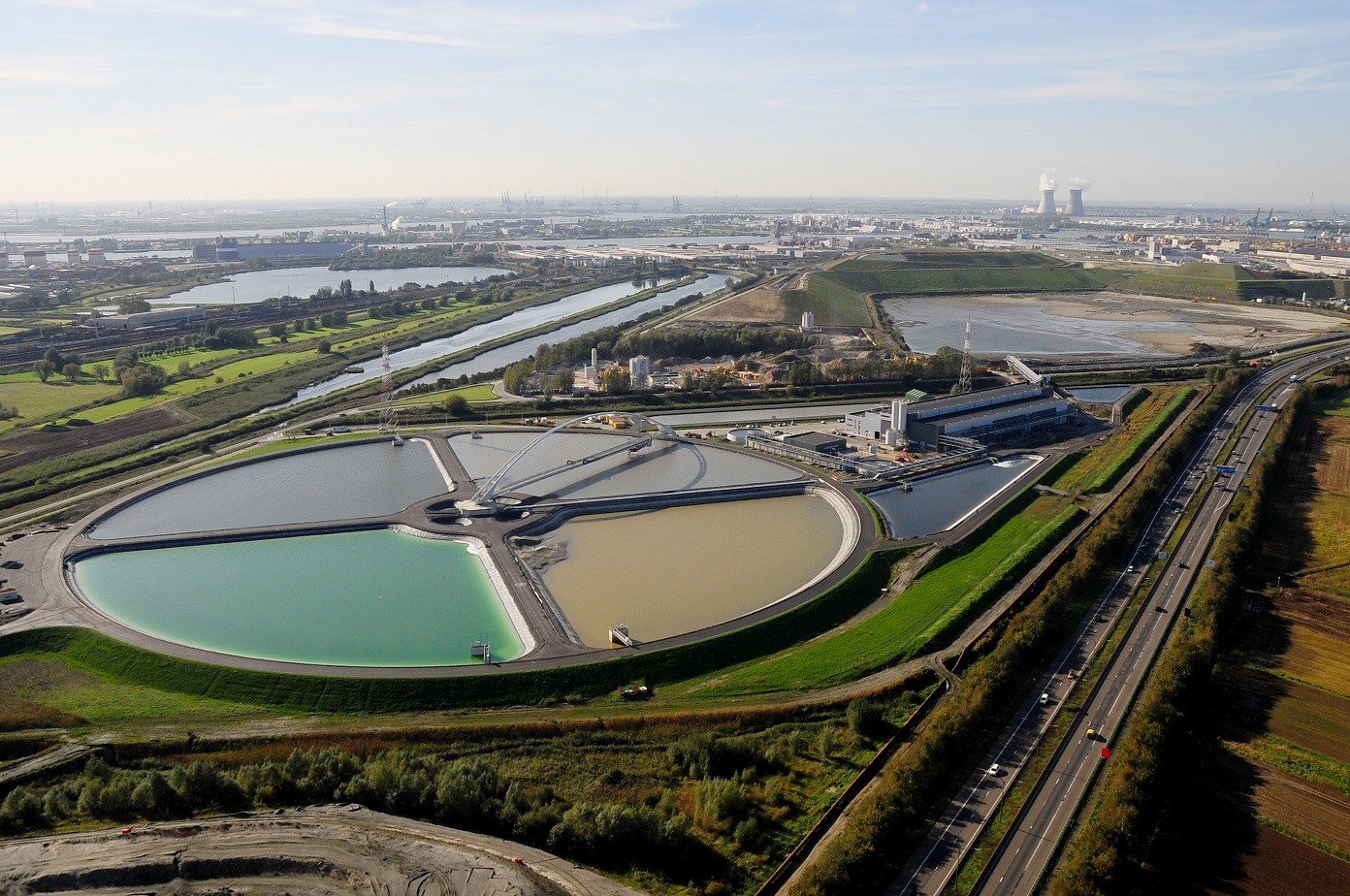 01 - (c)DMOW - Luchtfoto van AMORAS. Op de voorgrond zie je de indikvijvers met boogbrug, rechts daarachter de fabriekshal en vervolgens de stortplaats.