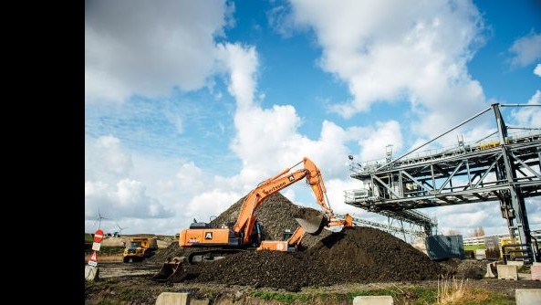 Stortplaats. Een kraan schept filterkoeken op om dumpers mee te beladen
