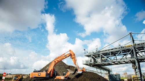 Stortplaats. Een kraan schept filterkoeken op om dumpers mee te beladen